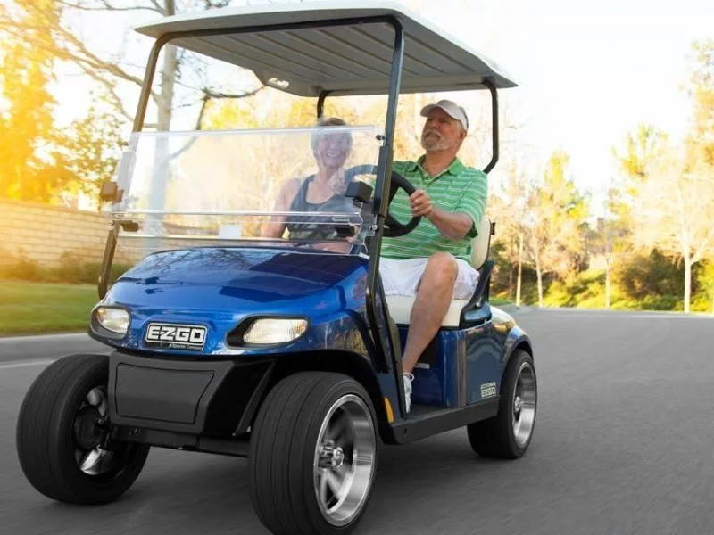 An elderly couple driving a blue EZGO golf cart.